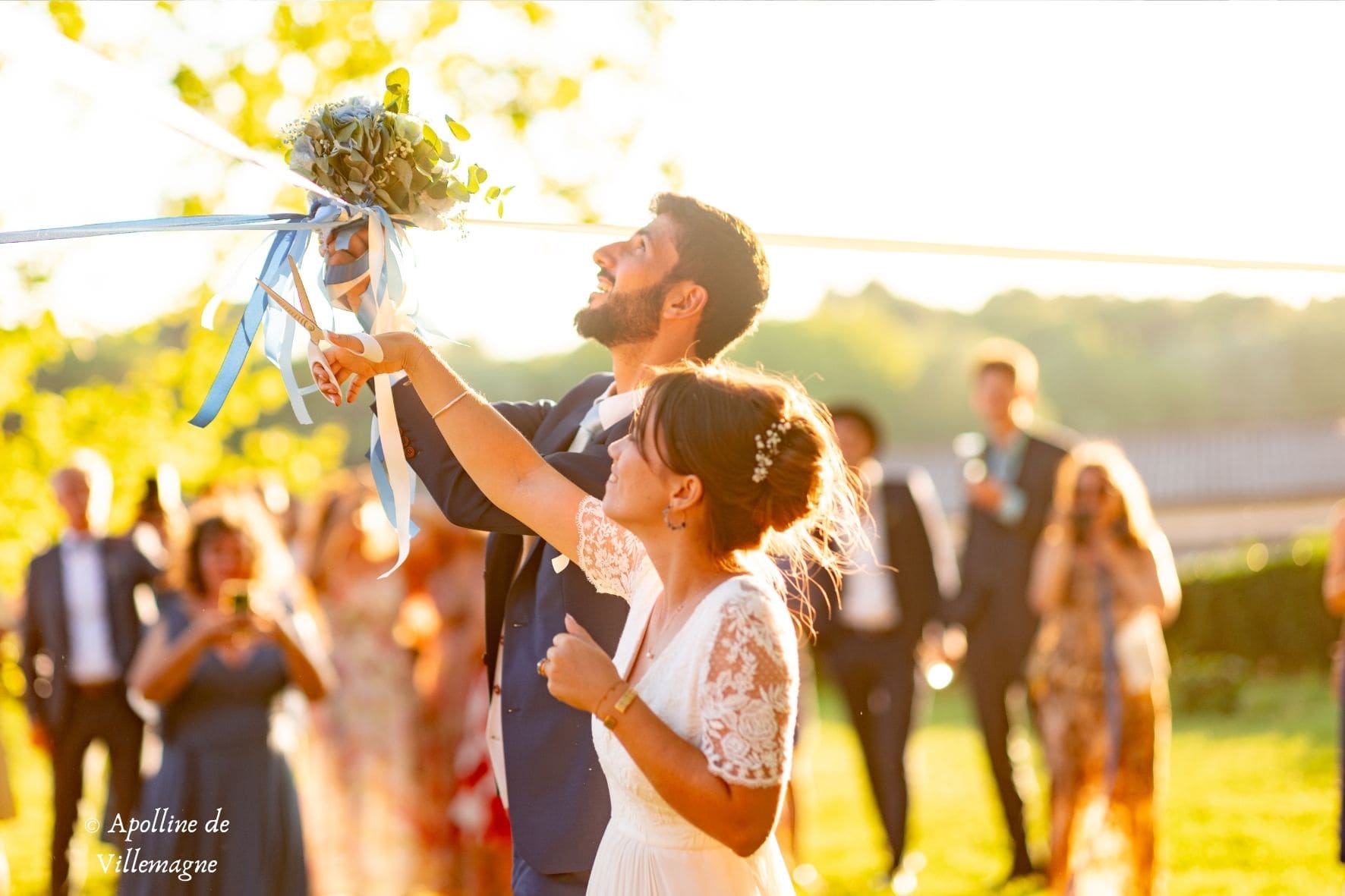 Couple souriant avec son bouquet et les invités en arrière-plan lors d’une cérémonie laïque